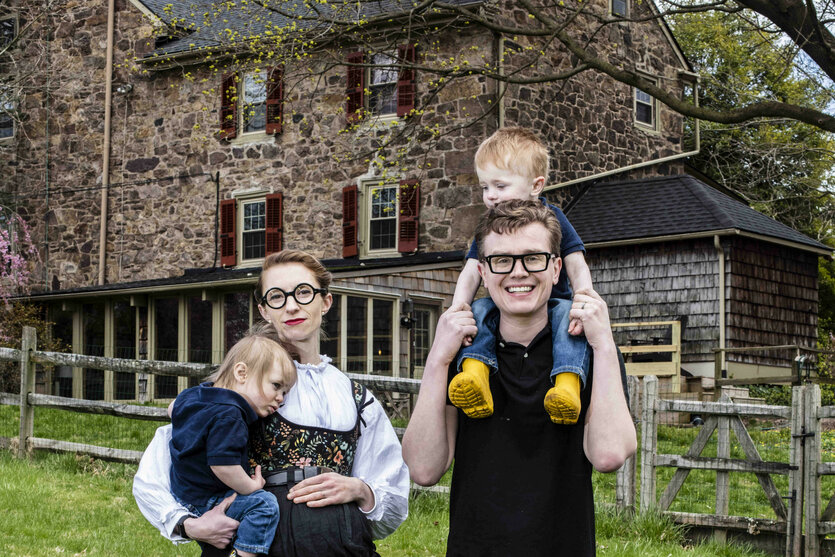 eine Familie mit kleinen Kindern auf dem Arm vor einem alten Haus