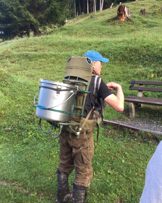 Eine Person trägt einen Behälter auf dem Rücken.