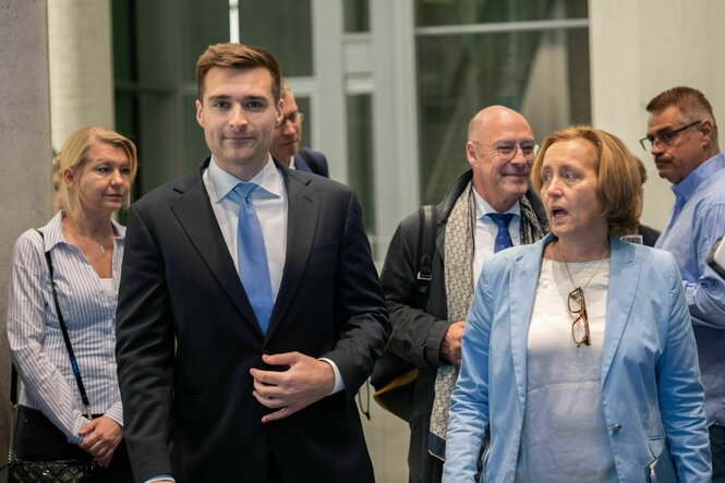 Alex Bruesewitz im schicken Anzug wird von Beatrix von Storch begleitet, ihr hängt die Brille um den Hals - im Hintergrund stehen mehrere Menschen