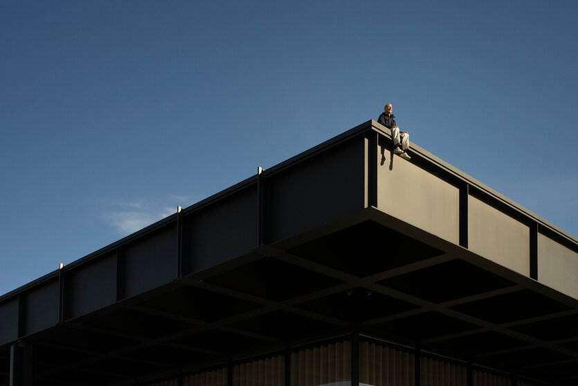 Maurizio Cattelan auf dem Dach der Neuen Nationalgalerie, schräg von hinten fotografiert