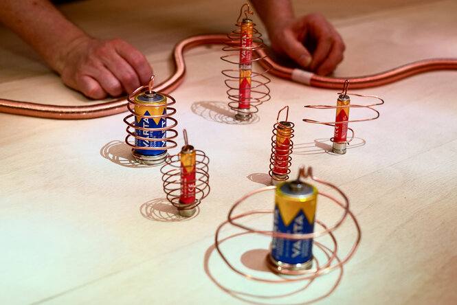 Ein paar Hände auf einem Tisch, davor mehrere Batterien in Drahtspiralen