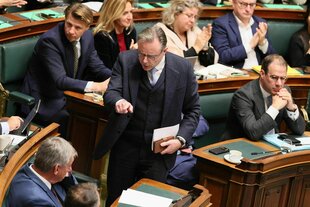 Der Premierminister Bart De Wever steht im Plenarsaal zwischen den besetzten Reihen und zeigt auf ein Schriftstück