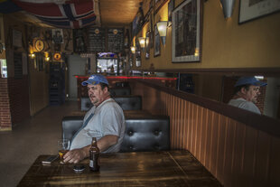 Ein Mann sitzt mit einer Flasche Bier an einem Tisch in einer leeren Bar