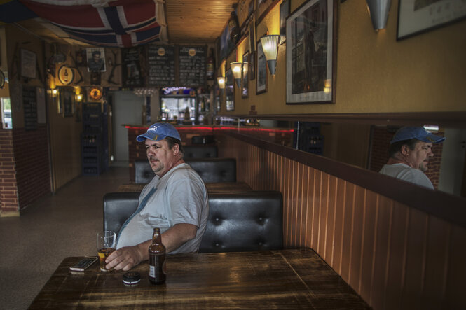 Ein Mann sitzt mit einer Flasche Bier an einem Tisch in einer leeren Bar
