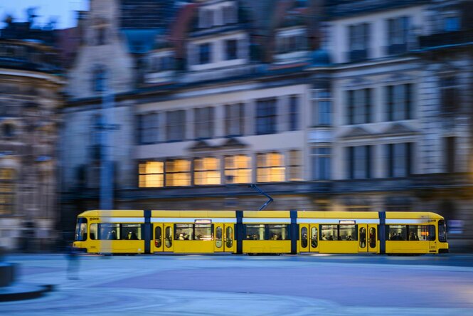 Eine gelbe Straßenbahnfährt in der Dämmerung durch die Stadt,der Platz davor ist sauber und die historischen Fassaden pittoresk