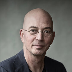 Tommy Wieringa sitzt in grauem Anzug auf einem Hocker