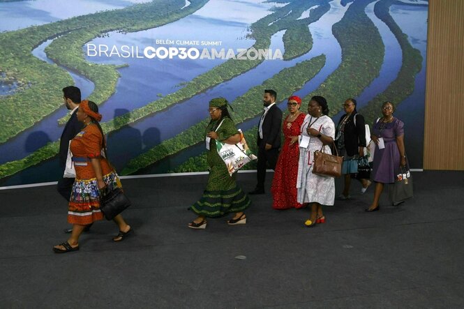 Eine Teilnehmergruppe in bunter Kleidung - die Männer im üblichen Anzug - betritt das Konferenzgebäude