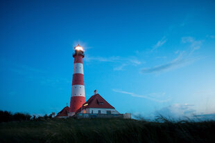 Ein Haus am Wattenmeer bei Dämmerung, im Hintergrund ein Leuchtturm