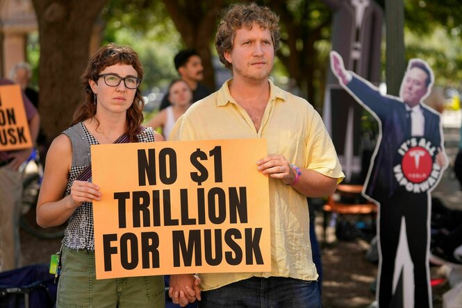 Zwei Personen halten ein Protestschild, auf dem steht: NO $1 TRILLION FOR MUSK