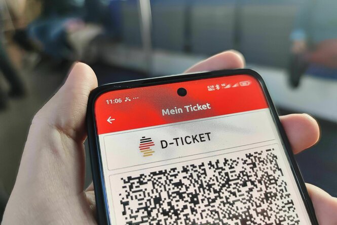 Eine Person hält ein Handy in der Hand, auf dem Display ist das Deutschlandticket als QR-Code zu sehen