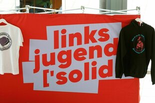 Ein T-shirt und ein Hoody hängen an einem Stand der Linksjugend 'Solid