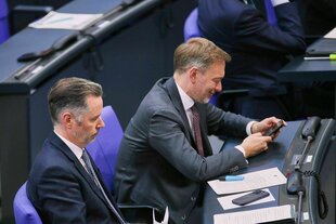 Christian Dürr sitzt schlecht gelaunt neben einem lächenlnden, Smartphone rumspielenden Christian Lindner, der auch noch grinst