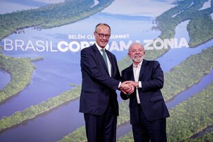 Kanzler Merz und Brasiliens Präsident Lula reichen einander die Hände vor einem riesigen Foto des Amazonas mit dem Schriftzug "BrasilCOP30Amazonia"