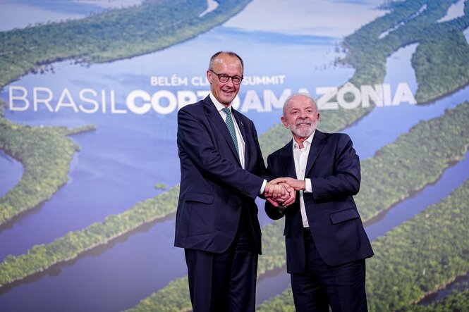 Kanzler Merz und Brasiliens Präsident Lula reichen einander die Hände vor einem riesigen Foto des Amazonas mit dem Schriftzug "BrasilCOP30Amazonia"