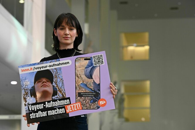 Yanni Gentsch steht mit einem Plakat in Leipzig in einem Gebäude - auf dem Plakat wird gefordert: Voyeur-Aufnahmen strafbar machen Jetzt !