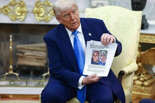 Donald Trump sitzt im Oval Office und hält ein Papier in die Kamera, das die Fotos von zwei Frauen zeigt, die verletzt sind