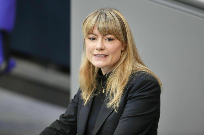 Clara Bünger steht am Rednerpult im Bundestag, sie trägt ein schwarzes Jacket und hat lange blonde Haare