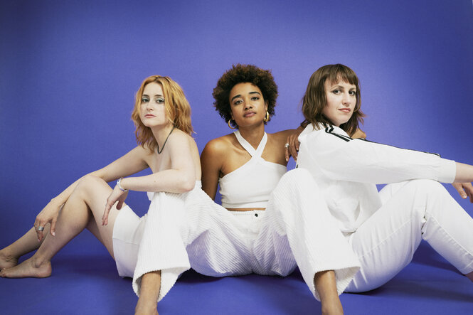 Drei junge Frauen in Weiß sitzen vor blauem Hintergrund