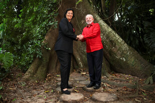 Die surinamische Präsidentin Jennifer Geerlings-Simons steht mit Präsident Lula unter einem Baum, sie halten sich an den Händen