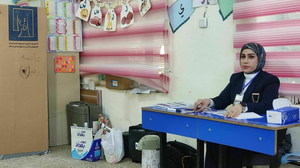 Eine Wahlhelferin sitzt an einem Tisch im Wahllokal, das sich in einer Schule befindet - an der Wand lehnt eine Wahlkabine aus Pappe