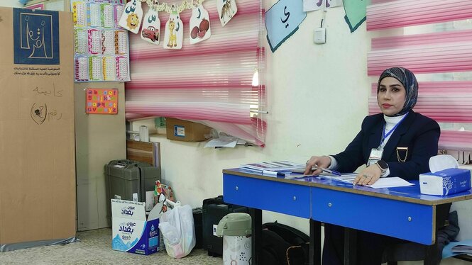 Eine Wahlhelferin sitzt an einem Tisch im Wahllokal, das sich in einer Schule befindet - an der Wand lehnt eine Wahlkabine aus Pappe