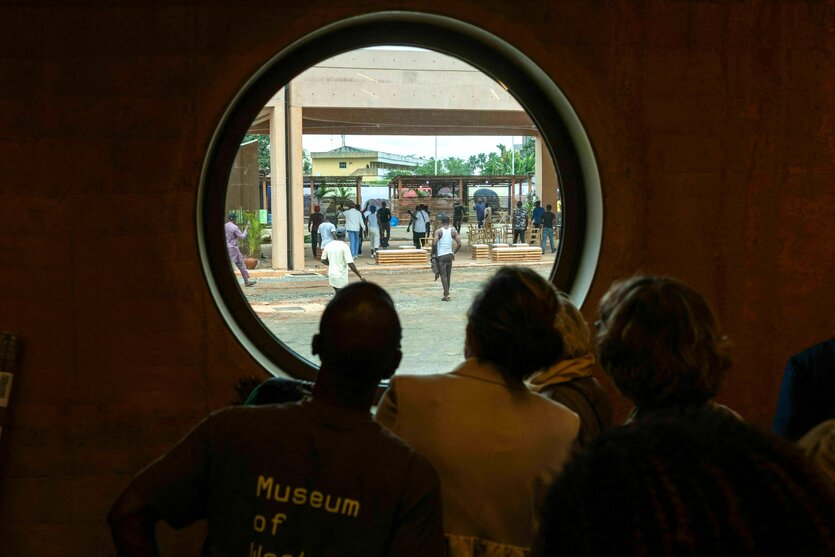 Mitarbeiter des Museums schauen durch ein rundes Fenster und beobachten dabei Männer, die sich auf dem Weg ins Museum befinden