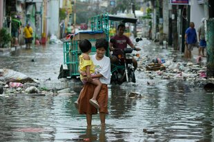 eine Frau mit einem Kind auf dem Arm auf einer überschwemmten Straße