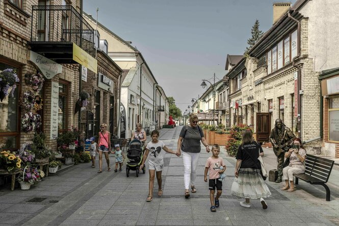 Fußgängerzone in Suwalki, Frauen mit Kindern an der Hand unterwegs, Blumengeschäft, eine Frau sitzt auf der Bank, hinter ihr ein bronzene Figur, die einen Straßenmusiker darstellt