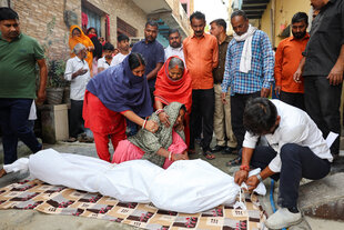Menschen stehen trauernd um ein in ein weißes Tuch eingewickeltes Todesopfer
