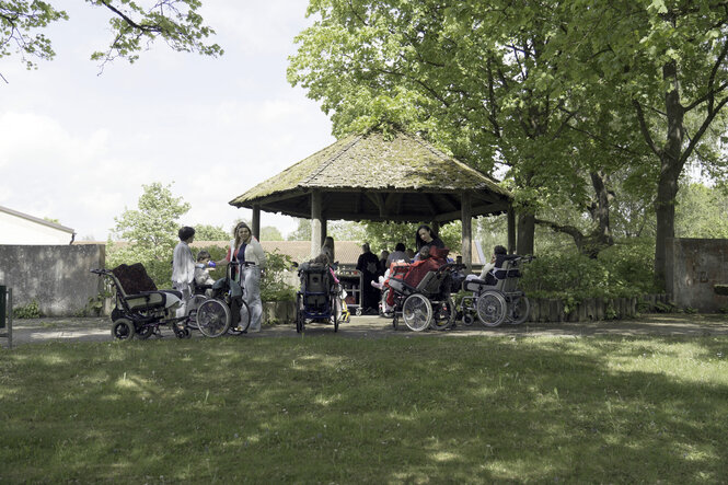 Unter einem Pavillon im Grünen sitzt eine Menschengruppe