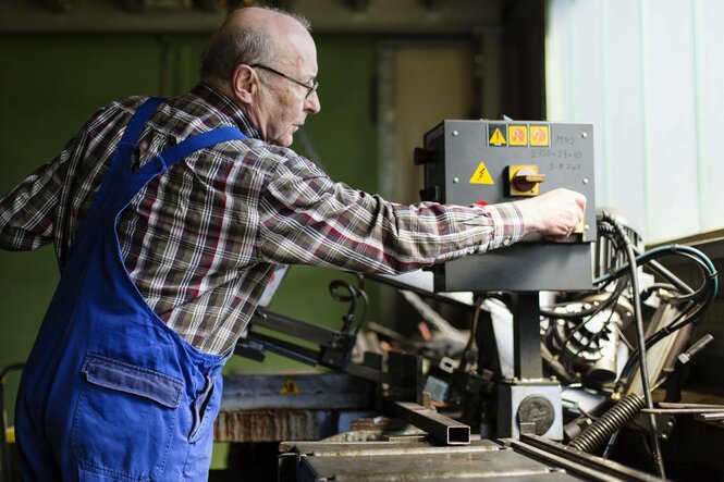 Eine ältere Person arbeitet an einer Werkbank.