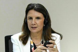 Porträt von Ana Toni, mit Kopfhörer und dem Smartphone in der Hand. Sie hat lange, dunkle Haare, trägt ein helles Jacket und Perlenketter