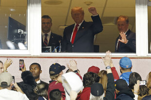 Drei Männer in einer Loge, davor Publikum. Trump ballt eine Faust