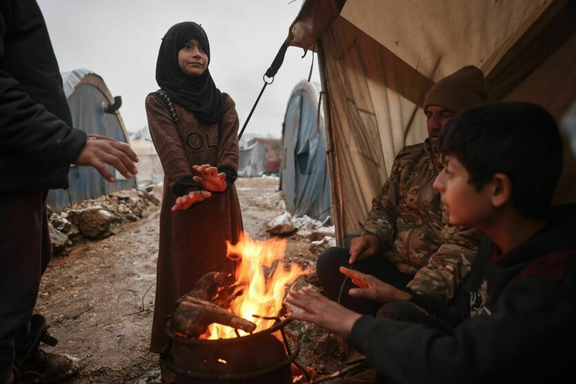 Menschen wärmen sich an einem Feuer außerhalb ihrer Zelte in einem schneebedeckten Lager