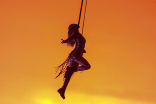 Helene Fischer schwebt mit ausgebreitetem Armen an einem Trapez vor orange-gelber Kulisse