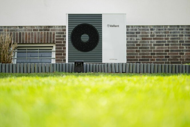 Eine Wärmepumpe vor einer Hauswand und hinter grünem saubern Rasen