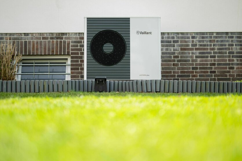 Eine Wärmepumpe vor einer Hauswand und hinter grünem saubern Rasen