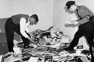 Zwei Personen in der Uniform der SA stehen auf einem Haufen Bücher und Broschüren