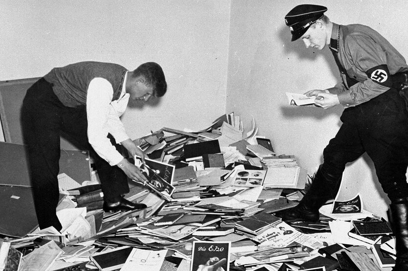 Zwei Personen in der Uniform der SA stehen auf einem Haufen Bücher und Broschüren