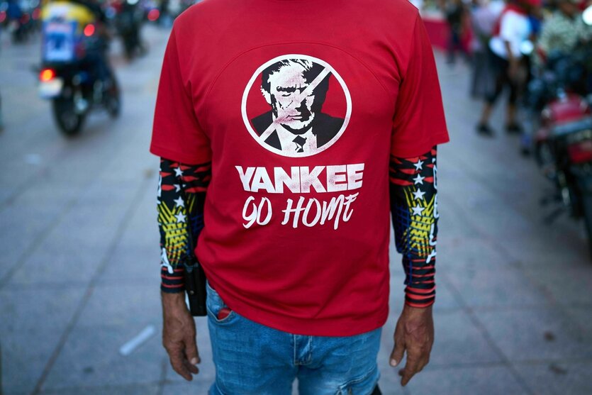 Ein Mann dessen Kopf nicht zu sehen ist, trägt ein rotes T-Shirt mit der Nachricht: Yankee go home und einem Porträt von Donald Trump, dessen Kopf durchgestrichen ist