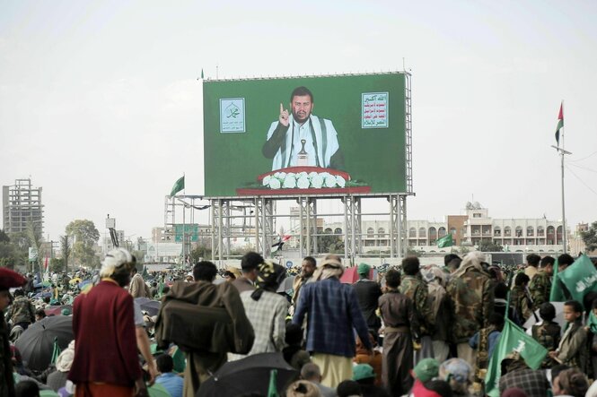 Auf einem Videoscreen ist ein Mann zu sehen, der mit dem Zeigefinger in die Höhe zeigt, es ist Abdulmalik al-Huthi