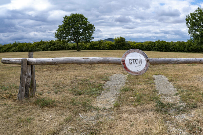 Ein hölzerner Schlagbaum auf trockerner Wiese mit einem Schild auf kyrillisch "Stop"