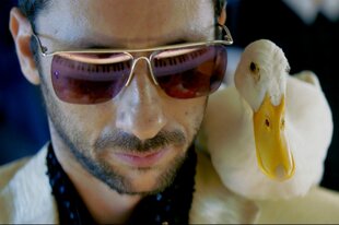 Ein Mann mit Sonnenbrille trägt eine Ente auf der Schulter