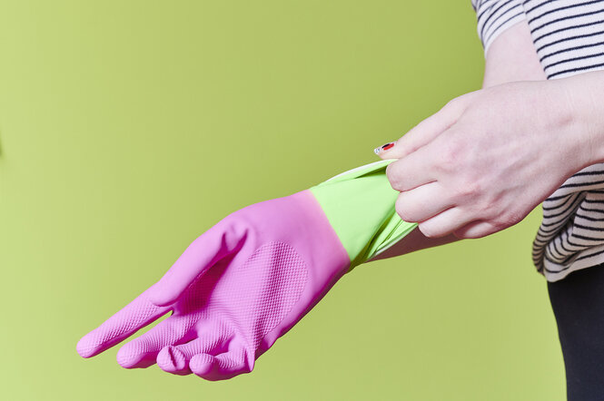 Eine Hand zieht einen pinkfarbenen Putzhandschuh über die andere