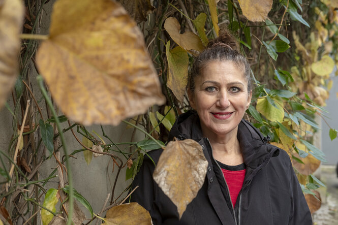 Eine Frau steht an einer Hauswand, die mit einer Kletterpflanze beqwachsen ist. Deren Blätter haben sich herbstlich verfärbt