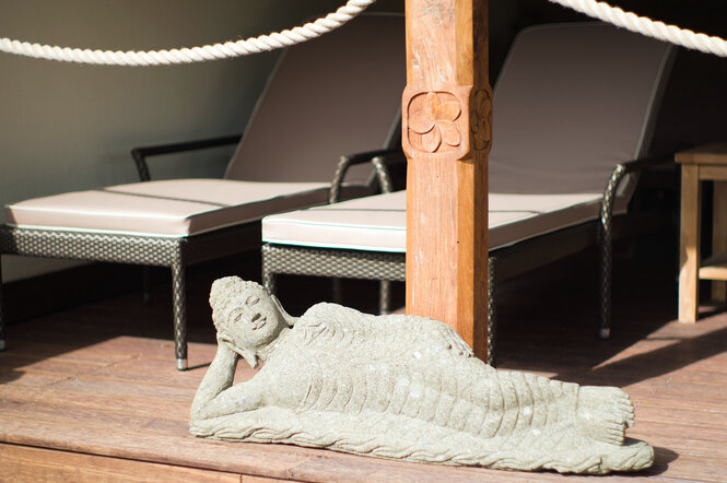 Eine asiatische Steinfigur vor Wellnessliegen