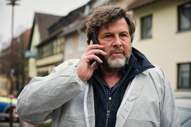 Ein Mann mittleren Alters mit Handy am Ohr vor einer süddeutsch anmutenden Stadtszene