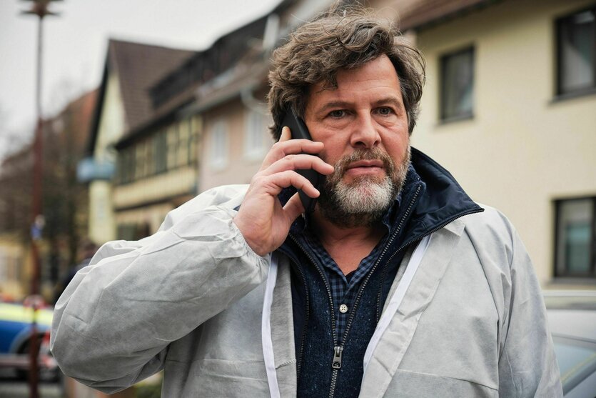 Ein Mann mittleren Alters mit Handy am Ohr vor einer süddeutsch anmutenden Stadtszene