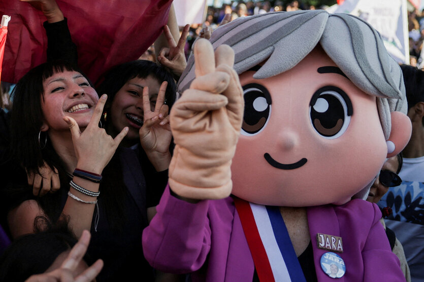 Eine als Jeannette Jara verkleidete Person gestikuliert mit anderen Personen