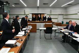 Blick in den Verhandlungsraum, Männer und Frauen in schwarzen Roben stehen vor ihren Tischen